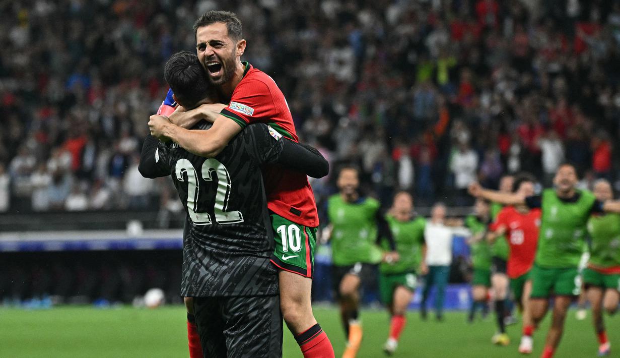 Kiper Portugal, Diogo Costa (kiri) dan Bruno Fernandes merayakan kemenangan atas Slovenia pada babak adu penalti saat babak 16 besar Euro 2024 di Frankfurt Arena, Frankfurt, Jerman, Senin (02/07/2024) WIB. (AFP/Javier Soriano)