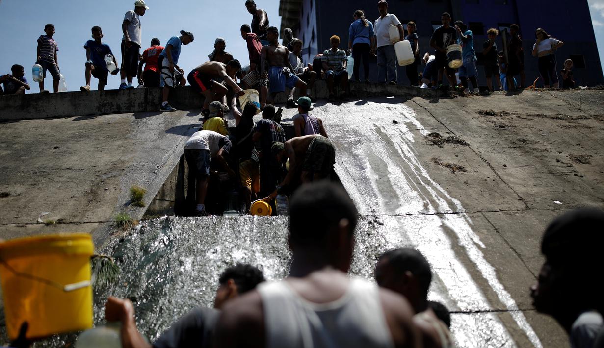 Orang-orang mengumpulkan air yang keluar melalui saluran pembuangan air limbah yang mengalir ke Sungai Guaire di Caracas, 11 Maret 2019. Pemadaman listrik selama berhari-hari di Venezuela berdampak terhadap krisis air. (REUTERS/Carlos Garcia Rawlins)