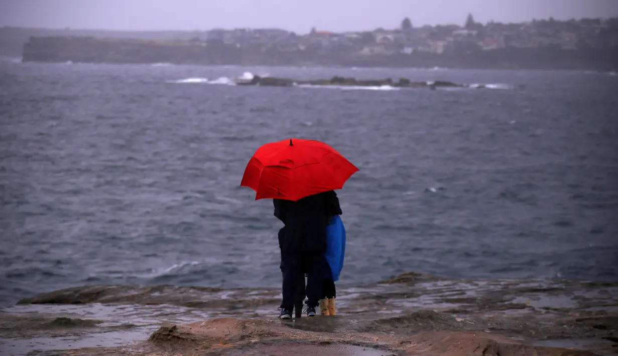 Warga menggunakan payung sambil menunggu untuk melihat kemunculan paus bungkuk ke permukaan Pantai Clovelly, Sydney, Australia, Minggu (19/6). (REUTERS/David Gray)