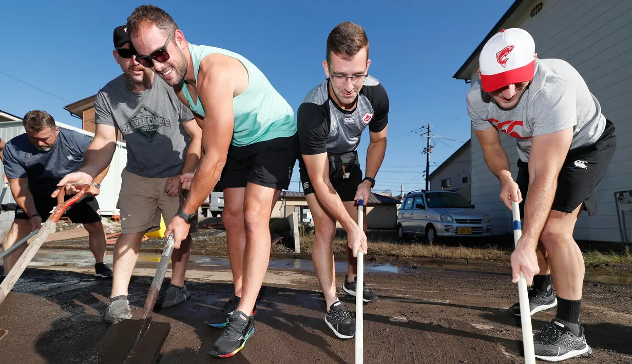 Para pemain rugby Kanada secara sukarela membersihkan jalan usai terjadi Topan Hagibis di Kamaishi, Prefektur Iwate, Jepang, Minggu (13/10/2019). Topan Hagibis membuat pertandingan Rugby World Cup Pool B antara Kanada dengan Namibia dibatalkan. (Kyodo News via AP)
