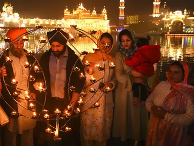 Umat Sikh menyalakan lampu tanah di Kuil Emas yang diterangi pada peringatan kelahiran Guru Nanak di Amritsar, India, 19 November 2021. Guru Nanak adalah Guru Sikh pertama dan pendiri Sikhisme. (AP Photo/Prabhjot Gill)