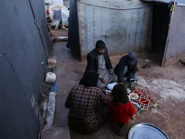 Pengungsi Suriah berkumpul di depan tenda untuk berbuka puasa dengan makanan yang didistribusikan organisasi amal lokal selama bulan suci Ramadhan, di kamp pengungsi di pinggiran kota Dana yang dikuasai pemberontak, timur perbatasan Turki-Suriah di Idlib (3/4/2022). (AFP/Aaref Watad)