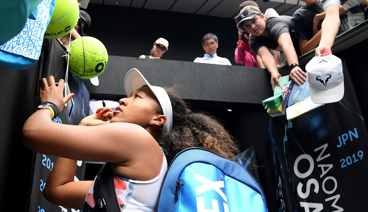 Petenis Jepang Naomi Osaka menandatangani benda yang disodorkan penonton usai mengalahkan petenis Republik Ceko Marie Bouzkova pada Australia Terbuka di Melbourne, Australia, Senin (20/1/2020). Penonton menyodorkan topi, bendera, hingga bola untuk ditandatangani Naomi. (AP Photo/Andy Brownbill)