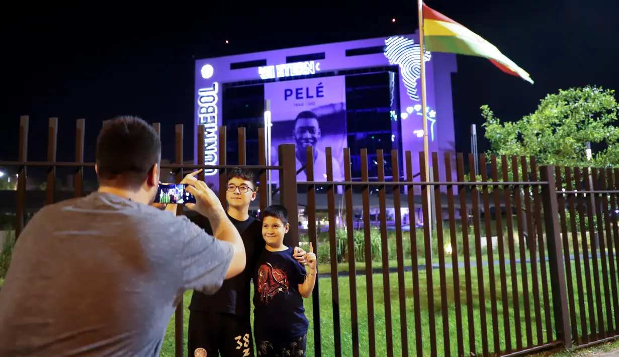 Seorang pria mengambil foto anak-anak dengan gambar mendiang legenda sepak bola Pele yang ditampilkan pada gedung markas CONMEBOL sebagai latar belakang di Luque, Paraguay, 29 Desember 2022. Pele yang memenangkan rekor tiga Piala Dunia, meninggal dunia pada usia 82 tahun. (AP Photo/Marta Escurra)