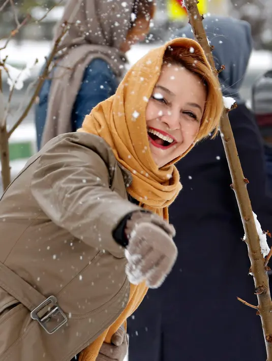 Seorang wanita melempar salju di Teheran, Selasa (24/1). Hampir setengah abad salju tak turun di Iran dan sejak 2011 hingga kini salju senantiasa turun di musim dingin. (AFP PHOTO / ATTA KENARE)   