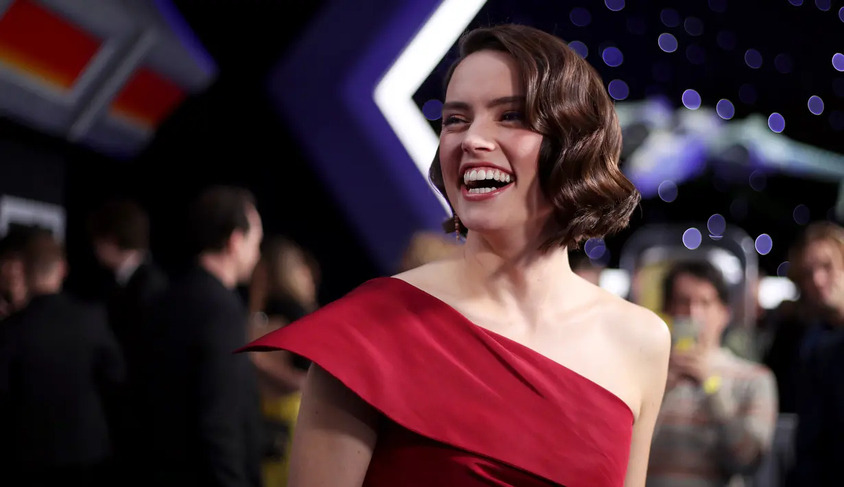 Aktris Daisy Ridley tertawa saat menghadiri pemutaran perdana film Disney "Star Wars: The Rise Of Skywalker" di Hollywood, California (16/12/2019). Daisy Ridley tampil cantik mengenakan gaun one-shoulder sutra merah dengan belahan paha yang terlihat. (Rich Fury/Getty Images/AFP)