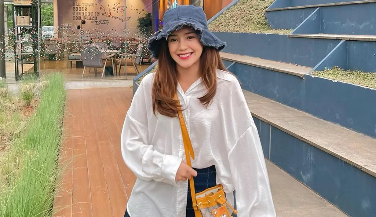 Memakai kemeja putih oversize yang dipadukan dengan rok serta bucket hat denim, penampilan kasual Beby Tsabina ini juga bisa ditiru. Dirinya pun menambahkan sling bag kuning sebagai detail penampilannya. (Liputan6.com/IG/bebytsabina)