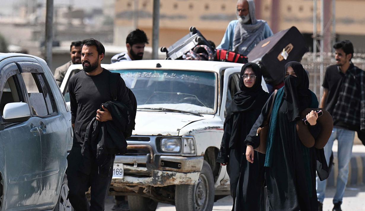 Dengan membawa koper-koper besar, mereka bergegas melintasi pintu gerbang logam di perbatasan antara Mirjaveh (Iran) dan Taftan (Pakistan). Warga Pakistan berjalan melintasi perbatasan Taftan, di provinsi Balochistan, Iran pada Selasa 3 Maret 2026, di tengah serangan Amerika Serikat dan Israel yang terus memanas. (Banaras KHAN/AFP)