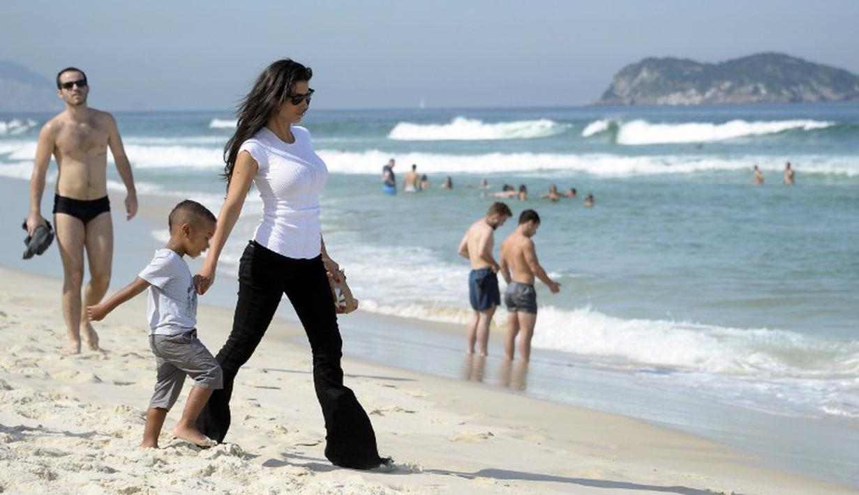 Ludivine Kadri memegang tangan buah hatinya saat berkunjung di Pantai Rio de Janeiro, Brasil (26/6/2014) (AFP PHOTO/FRANCK FIFE)