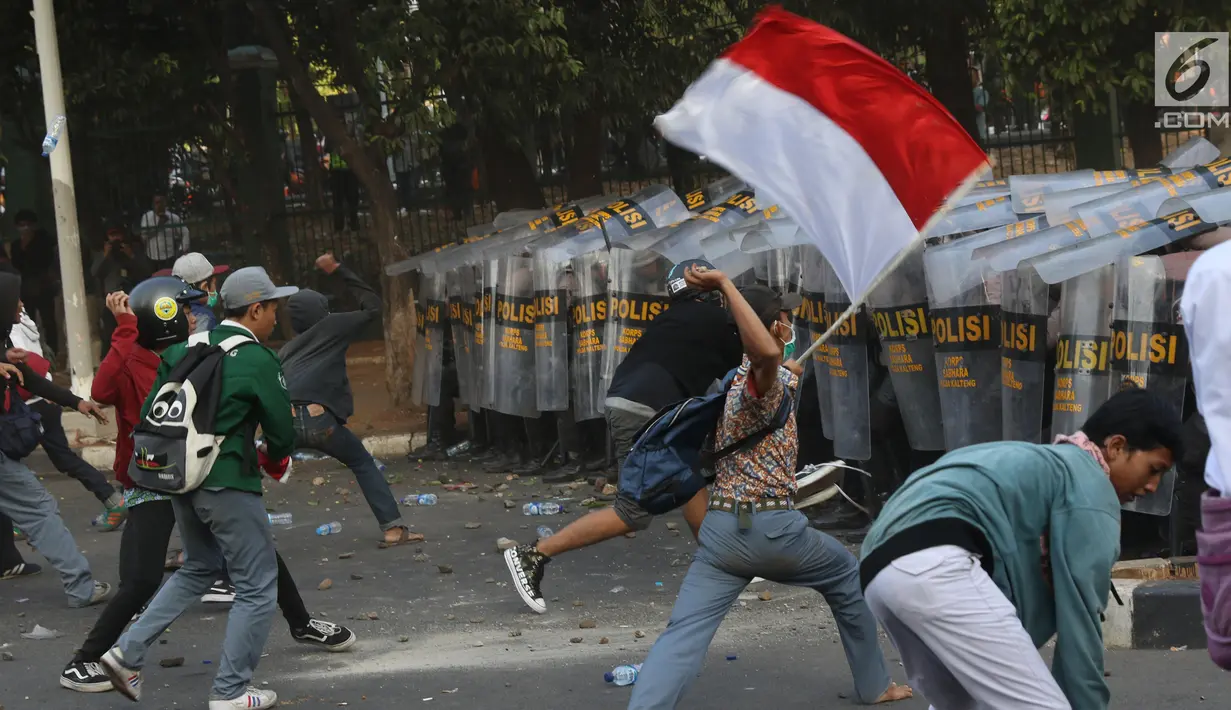 Massa melempar batu ke arah polisi yang membentuk barikade dengan tameng di sekitaran Gedung DPR RI, Jakarta, Senin (30/9/2019). Kericuhan pecah lantaran massa yang kebayakan terdiri dari pelajar tersebut berusaha masuk ke area depan DPR. (Liputan6.com/Angga Yuniar)