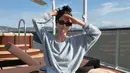 Pada salah satu foto, bintang The Glory itu terlihat duduk bersila di area sun deck mengenakan sweater abu-abu longgar yang dipadukan dengan celana linen biru muda. Rambutnya ditata dalam messy bun sederhana dan dilengkapi kacamata hitam berbingkai ramping. Tanpa aksesori berlebihan, tampilannya justru memancarkan kesan chic khas gaya liburan old money yang sedang digemari. [Dok/@kyo1122].