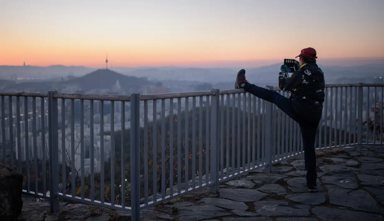 Seorang pejalan kaki mengabadikan kota Seoul dan menara Namsan dengan ponselnya selama matahari terbit di Korea Selatan (31/10). Seoul adalah ibu kota Korea Selatan yang berusia lebih dari 600 tahun. (AFP Photo/Ed Jones)