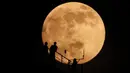 Siluet orang-orang saat bulan hampir purnama muncul di atas langit di Grozny, Rusia, Minggu (15/5/2022). (AP Photo/Musa Sadulayev)
