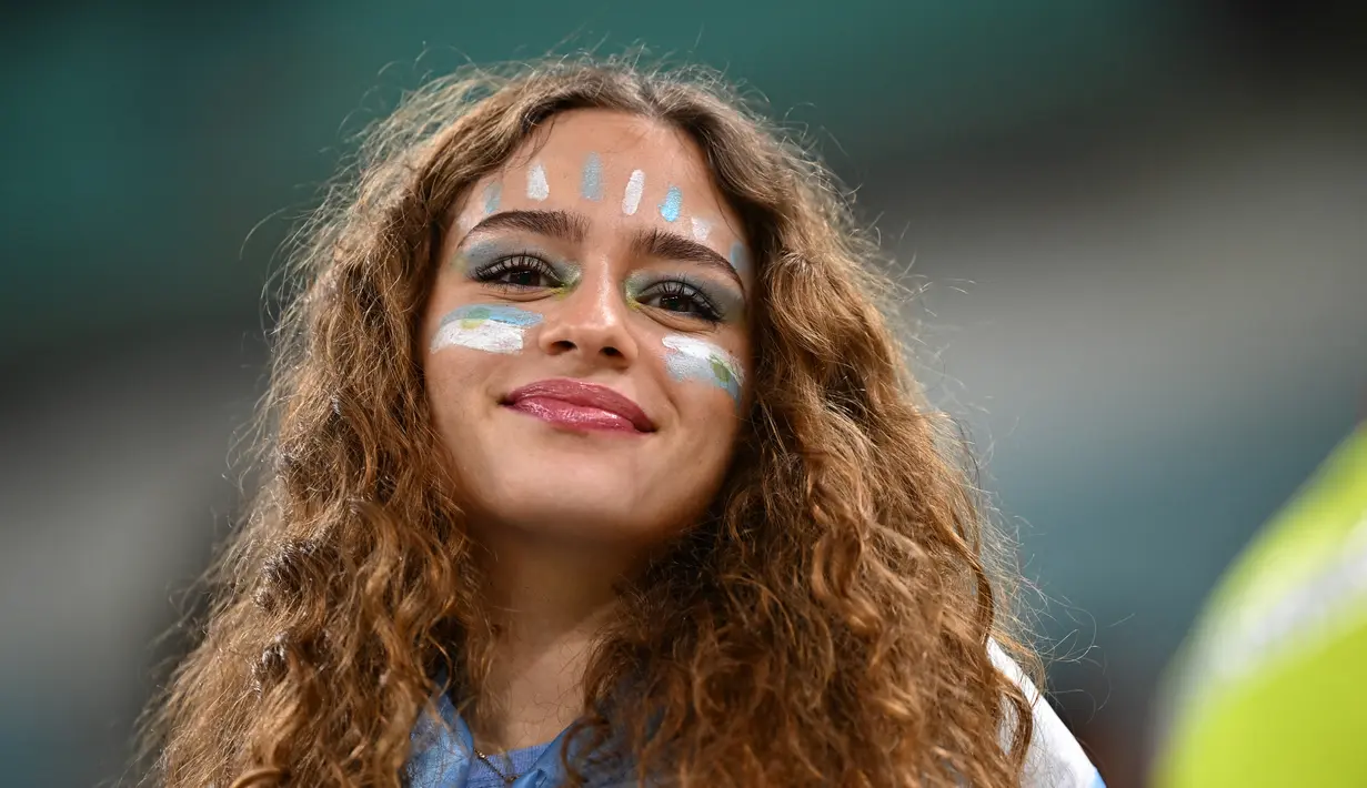 Seorang fans wanita Argentina tersenyum di tribun menjelang pertandingan semifinal Piala Dunia Qatar 2022 antara Argentina dan Kroasia di Stadion Lusail di Lusail, utara Doha, Rabu (14/12/2022). (AFP/ Anne-Christine Poujoulat)