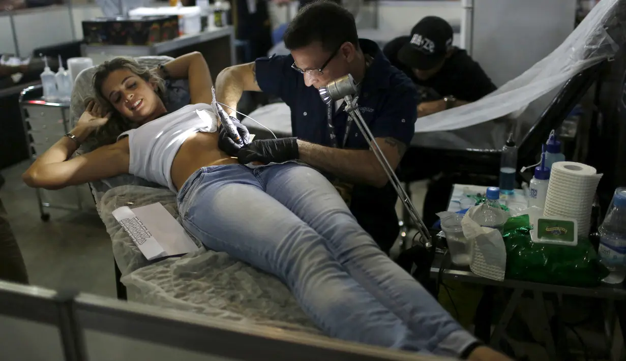 Seorang seniman saat menato seorang perempuan dibagian perutnya saat Festival Internasional Tattoo Week Rio 2016 ketiga di Rio de Janeiro, Brasil, (22/1/2016). (REUTERS/Pilar Olivares)