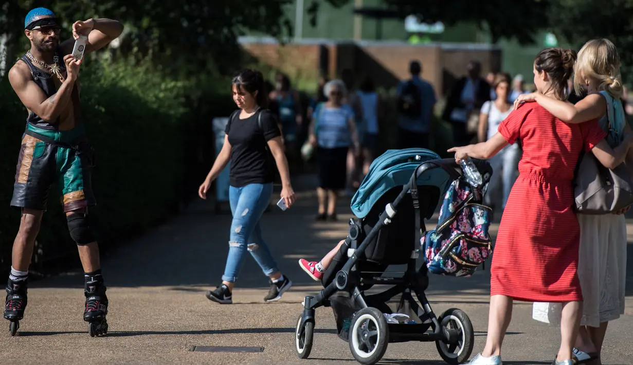 Seorang skater roller berhenti untuk mengambil foto dua wanita saat suhu musim panas mencapai sekitar 28 derajat di Hyde Park di London, Inggris (5/7). (AFP Photo/Chris J Ratcliffe)