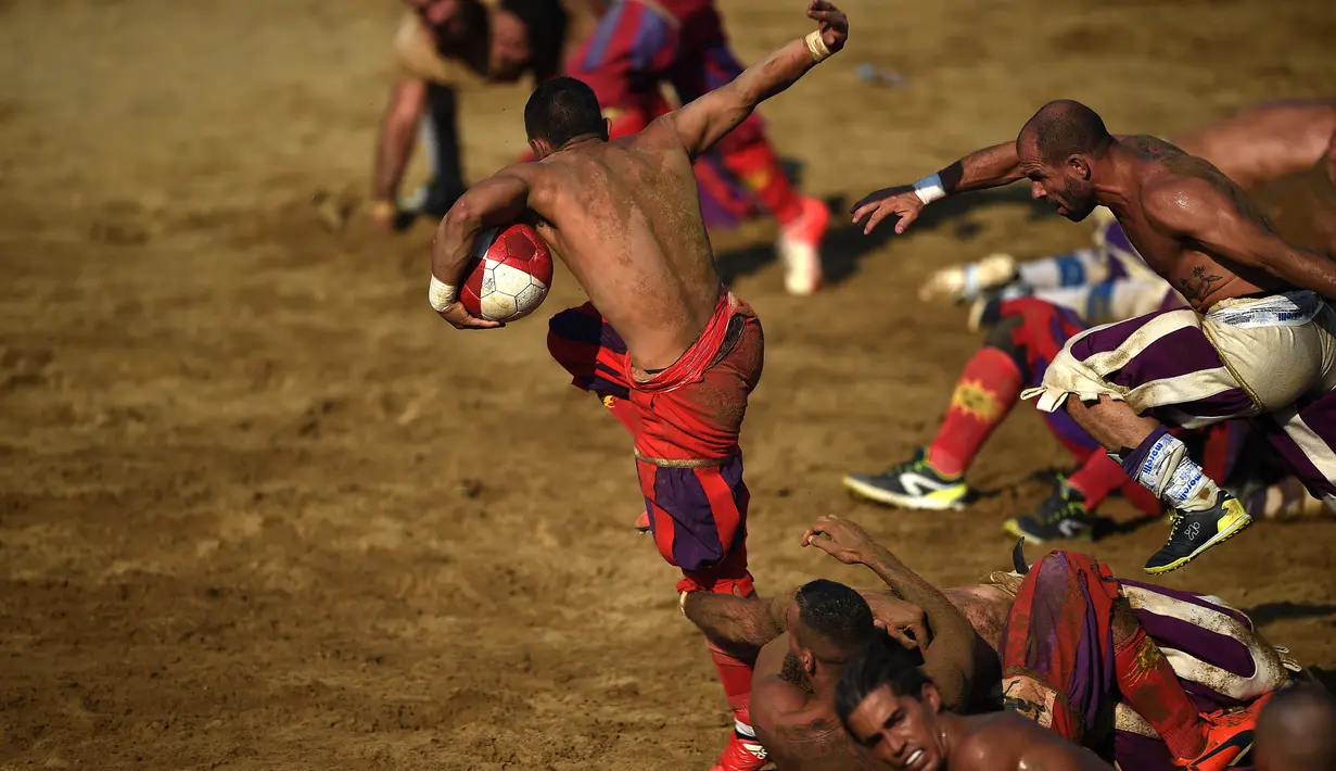 Seorang pemain membawa bola berusaha melewati lawannya saat pertandingan Calcio Storico Fiorentino di Piazza Santa Croce di Florence, Italia (24/6). (AFP Photo/Filippo Monteforte)