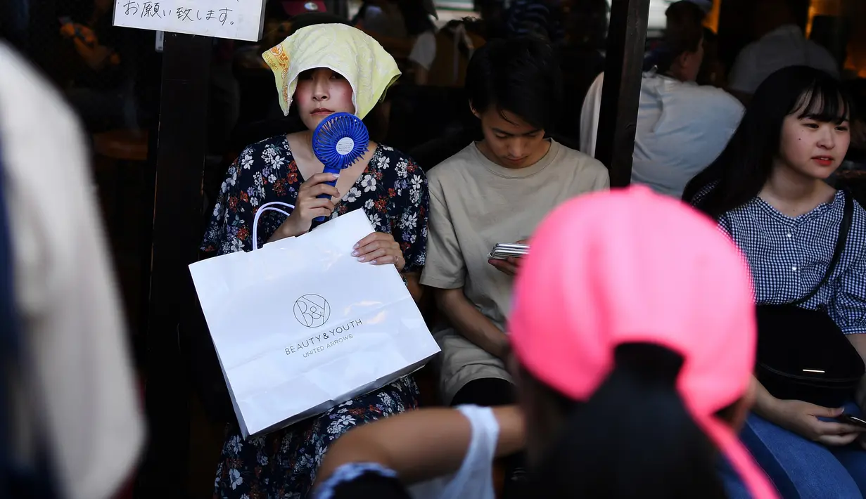 Seorang wanita memegang kipas portabel saat mengantre di depan sebuah restoran selama gelombang panas di distrik Shin-Okubo Tokyo, Minggu (4/8/2019). Setelah menyerang beberapa wilayah di Eropa, suhu tinggi juga terjadi di Jepang. (Charly TRIBALLEAU / AFP)