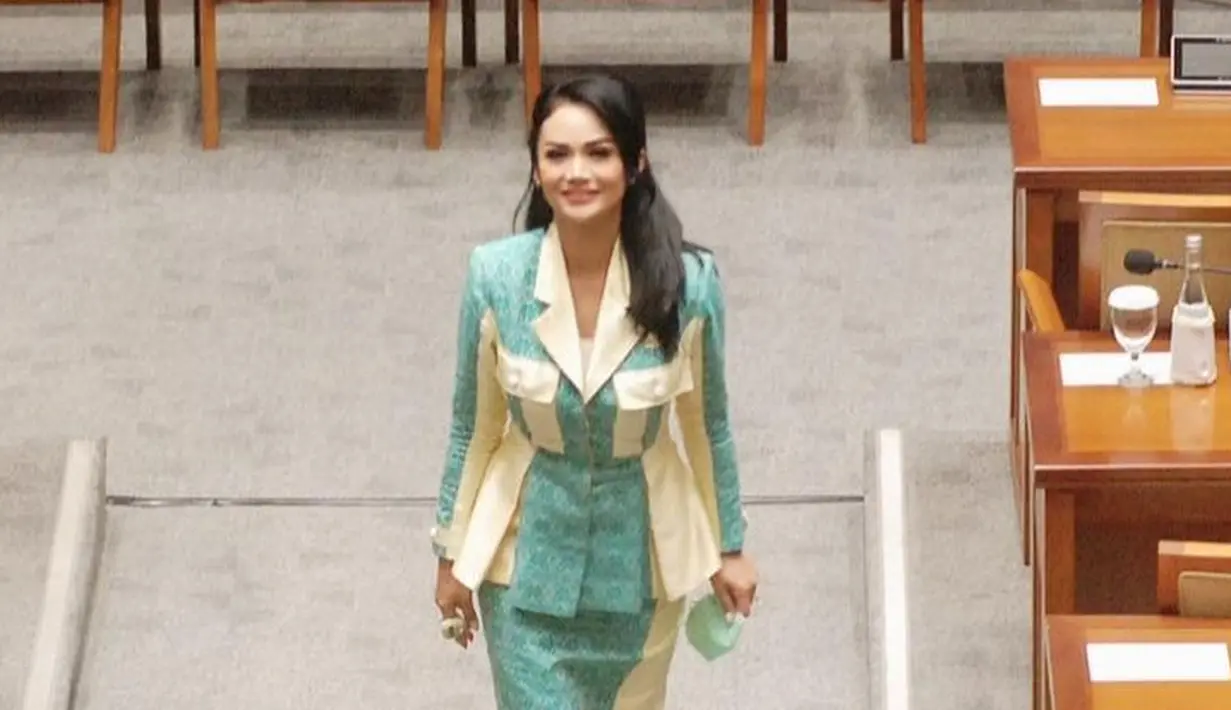 Busana etnik yang kontras juga pernah dikenakan Krisdayanti saat berkantor di DPR. Ia memilih memadukan kain bermotif warna biru muda dengan warna cream dalam potongan atasan blouse collar dan span skirt. Heels berwarna nude menjadi penutup cantik pada keseluruhan tampilan.