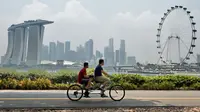 Dua orang bersepeda sambil mengamati skyline kota Singapura yang diselimuti kabut. Meskipun Singapura adalah kota dengan biaya hidup paling tinggi di dunia, namun biaya hidup di sana 10% lebih murah dibandingkan di New York. (AFP PHOTO/Roslan RAHMAN)