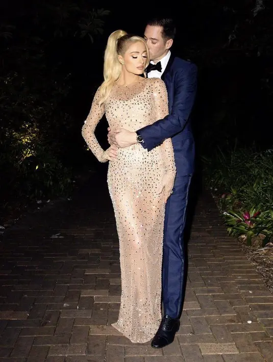 Paris tampil mengenakan gaun bodycon warna nude transparan dengan detail manik-manik. Sedangkan sang suami dengan setelan suitnya.(@parishilton)