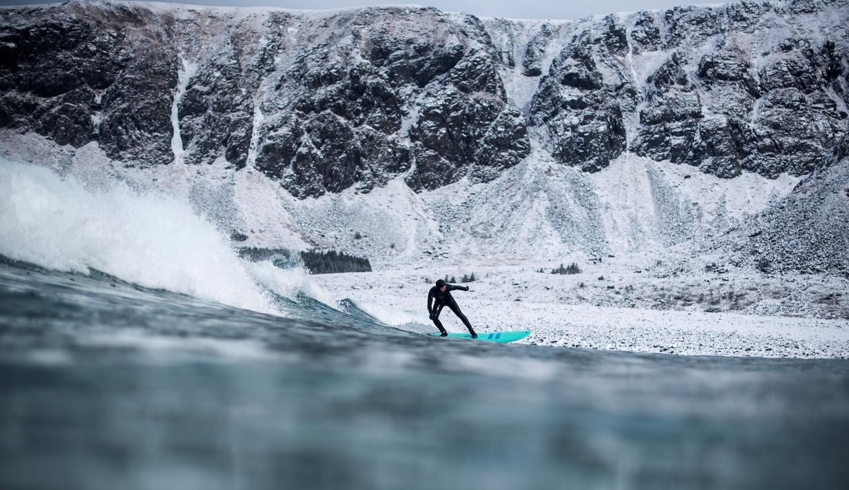 Aksi seorang peselancar diantara hamparan bukit es dan hawa dingin di Lofoten Islands, Norwegia, (10/3/2018). Suhu udara minus 13°C dan suhu diatas air sekitar 4°C. (AFP/Oliver Morin)