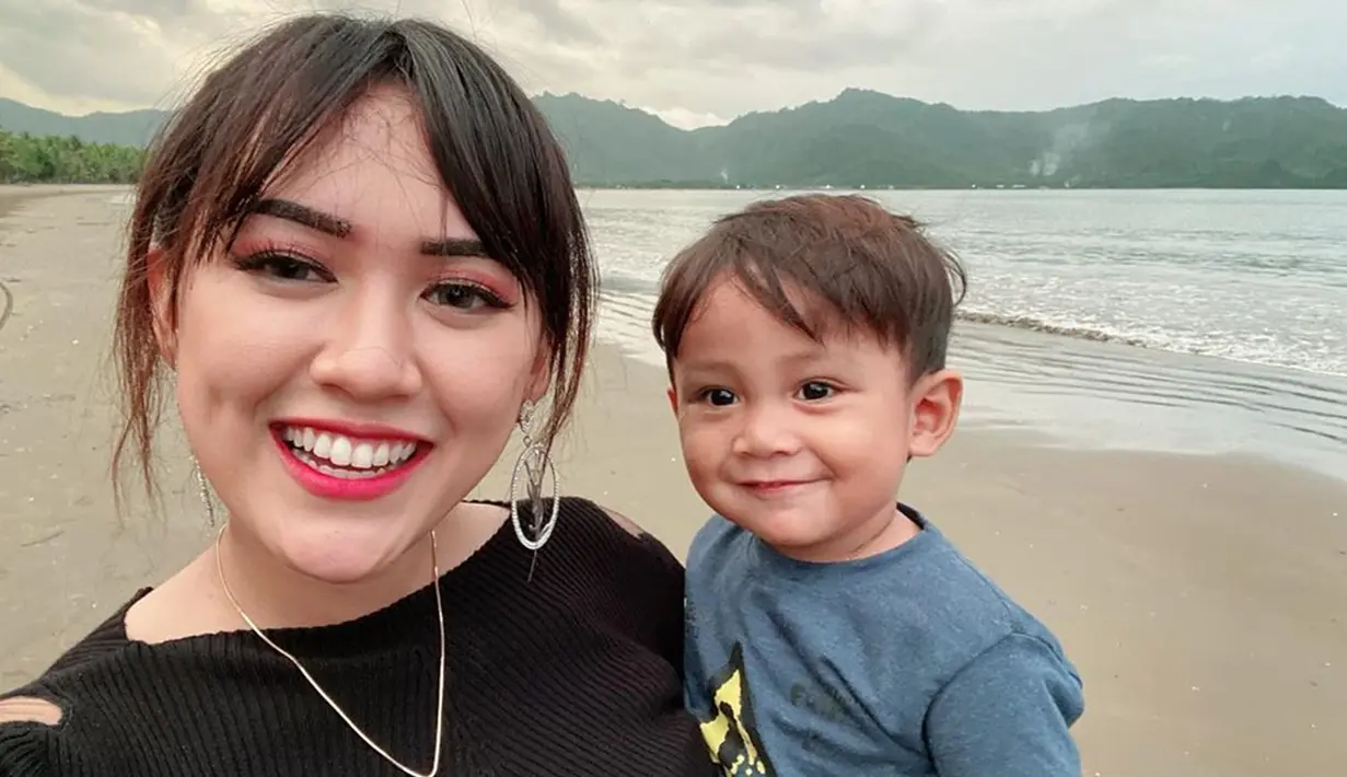 Kebahagiaan Happy Asmjara semakin lengkap saja saat berlibur ke pantai bersama sanak saudara. Ia menggendong mesra anak kecil dengan bahagianya. Raut wajah bahagia tersebut seperti semakin membuat keindahan pantai Kandat terlihat saja. (Liputan6.com/IG/happy_asmara77)