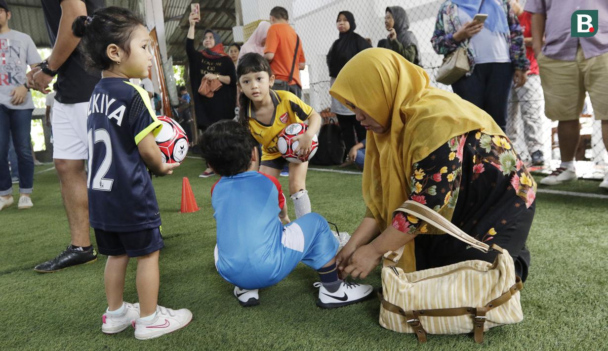 Seorang ibu memasang tali sepatu anak saat mengikuti latihan bersama Il Capitano Soccer School di Bintaro, Sabtu (27/10/2018). Kehadiran Il Capitano untuk menjaring dan mengasah pesepak bola cilik untuk berprestasi. (Bola.com/M Iqbal Ichsan)