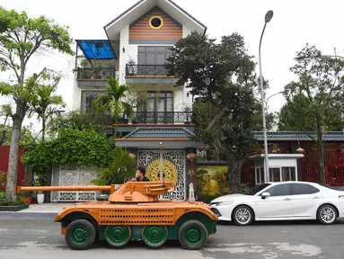 Truong Van Dao melewati sebuah rumah dengan tank kayu di daerah perumahan di provinsi Bac Ninh pada 28 Maret 2022. Seorang ayah di Vietnam telah menghabiskan ratusan jam dan menginvestasikan uangnya untuk mengubah mobil van tua menjadi tank kayu untuk putranya. (Nhac NGUYEN /AFP)