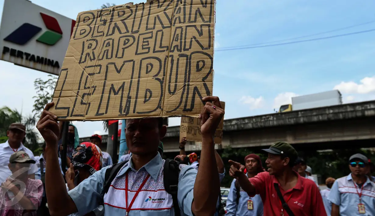 Seorang peserta aksi menunjukkan sebuah poster saat melakukan mogok kerja dan unjuk rasa di Depot Pertamina Plumpang, Jakarta, Selasa (1/11). Para Awak Mobil Tangki Pertamina menuntut perusahaan menghapus sistem outsourcing. (Liputan6.com/Faizal Fanani)