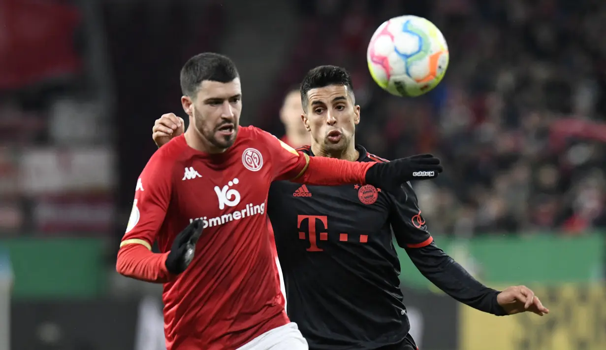 Bek Bayern Muenchen, Joao Cancelo berebut bola dengan bek Mainz 05, Aaron Martin selama pertandingan babak 16 besar Piala Jerman (DFB Pokal) di Mewa Arena, Mainz, Jerman (1/2/2023). MUusim lalu, Cancelo memiliki angka keterlibatan gol yang cukup bagus dalam kapasitasnya sebagai fullback kiri di skema permainan Manchester City. (AFP/Thomas Kienzle)