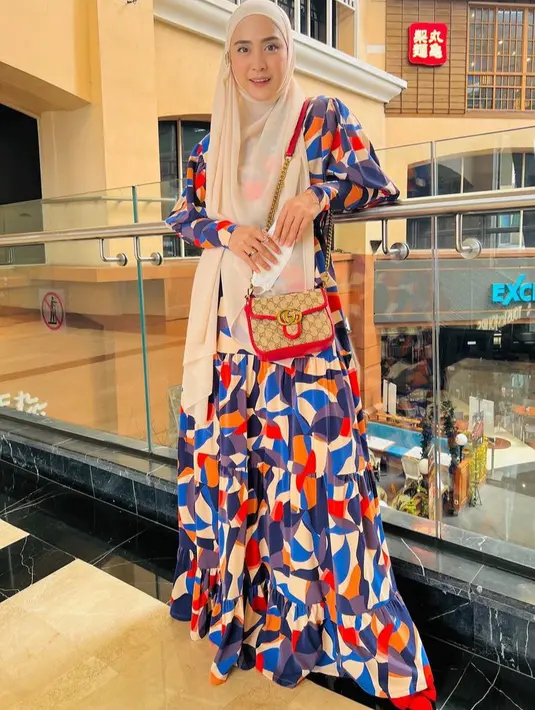 Ia juga tampil dengan kerudung coklat muda dipadukan dress bermotif colorful, sambil membawa sling bag Gucci.  [@apriljasmine]