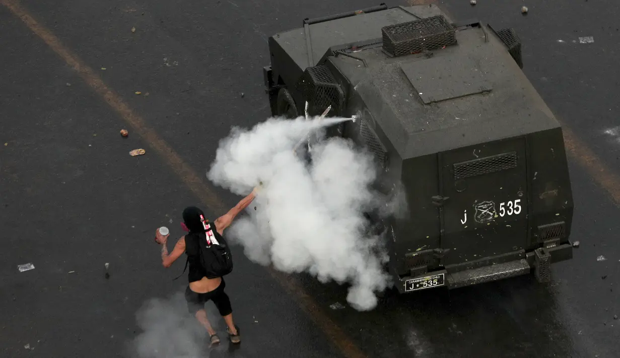 Demonstran melemparkan gas air mata ke arah kendaraan polisi di Santiago, Chile (4/10/2019). Pengunjuk rasa menuntut diakhirinya ketidaksetaraan ekonomi bahkan ketika pemerintah mengumumkan bahwa demonstrasi selama berminggu-minggu merugikan pertumbuhan ekonomi negara. (AP Photo/Esteban Felix)