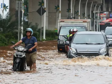 Pengendara terpaksa mendorong motornya saat melintasi genangan air di Jalan Boulevard Raya, Kelapa Gading, Jakarta, Rabu (29/1/2025). (Liputan6.com/Herman Zakharia)