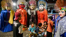 Foto pada 10 April 2019, anak-anak beristirahat dari mencari nafkah dengan mengamen ondel-ondel di jalan-jalan Jakarta. Seiring berjalan waktu, ondel-ondel yang dahulu sebagai ikon kesenian Betawi kini mudah ditemui di sejumlah jalan dan gang-gang di antara permukiman warga. (GOH CHAI HIN / AFP)