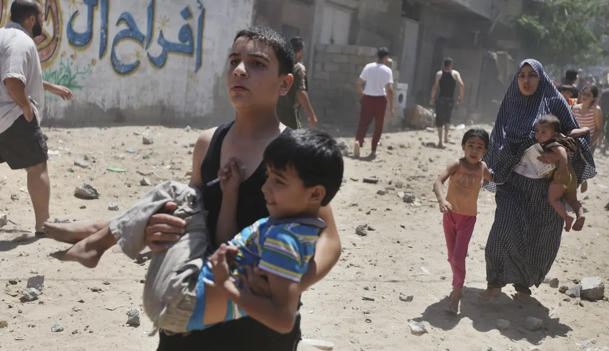 Pemuda Palestina menggendong adiknya berlari mencari tempat aman saat terjadi serangan udara Israel di Gaza, Rabu (9/7/14). (REUTERS/Majdi Fathi)