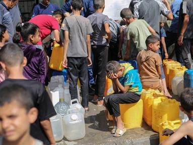 Anak-anak Palestina duduk di atas jeriken mereka sambil mengantre air di titik distribusi bantuan di kamp pengungsi Nuseirat, Jalur Gaza yang dikepung Israel pada 4 September 2025. (Eyad BABA/AFP)