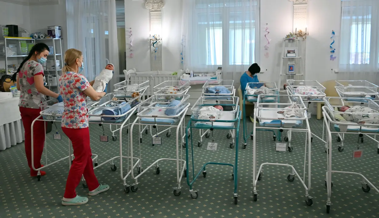 Perawat merawat bayi yang baru lahir dari skema ibu pengganti (surrogate mother) di Hotel Venice, Kiev, Ukraina, 15 Mei 2020. Para orangtua bayi tersebut belum dapat masuk ke Ukraina karena terkendala larangan bepergian. (Sergei SUPINSKY/AFP)