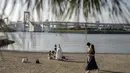 Orang-orang berjalan pada hari yang cerah di tepi teluk di daerah Odaiba Tokyo (12/4/2022). Para pengunjung biasanya datang ke Seaside Park untuk menikmati pemandangan Gunung Fuji dari bianglala Daikanransha dan berinteraksi dengan robot di museum sains Miraikan. (AFP/Charly Triballeau)