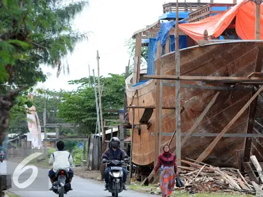 Warga melintas di area pembuatan perahu di Balongan, Indramayu, Jawa Barat, Jumat (15/1/2016). Dibutuhkan waktu selama delapan bulan untuk menyelesaikan satu unit perahu yang dijual seharga Rp.4 miliar - Rp.5 miliar tersebut. (Liputan6.com/Helmi Afandi)