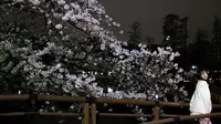 Seorang wanita berpose di samping bunga sakura yang bermekaran saat malam hari di Taman Inokashira di Tokyo, Jepang (29/3/2022). (AFP/Philip Fong)