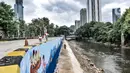 Warga melintas di dekat seniman yang tengah menyelesaikan pembuatan mural di turap Kanal Banjir Barat, Jakarta, Rabu (13/1/2021). Pembuatan mural ini bertemakan "Kehidupan Sungai" ini dikerjakan oleh seniman dari Komunitas Mural Depok. (merdeka.com/Iqbal S. Nugroho)