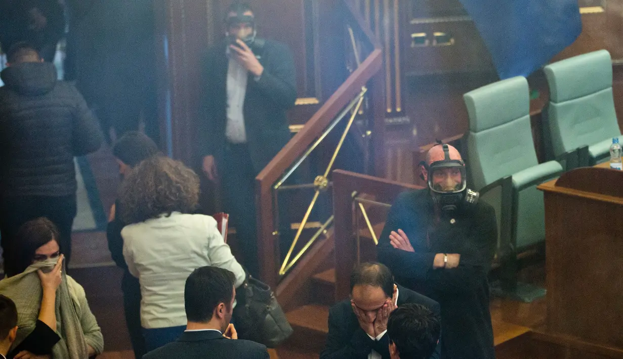 Petugas kepolisian mengenakan masker saat Para politisi meninggalkan ruangan yang dipenuhi asap gas air mata dalam rapat parlemen di ibu kota Kosovo, Pristina, Rabu (21/3). Ketua Parlemen Kadri Verseli terpaksa menunda sidang. (AP Photo/Visar Kryeziu)