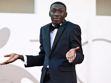 Khaby Lame berpose dengan ciri khasnya saat tiba untuk pemutaran film "Il Signore Delle Formiche" (Penguasa Semut) selama Venice Film Festival 2022 ke-79 di Lido di Venesia, Italia (6/9/2022). YouTuber Italia kelahiran Senegal ini tampil mengenakan tuxedo hitam di acara tersebut. (AFP/Tiziana Fabi)