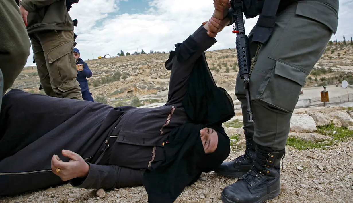 Polisi Israel membangunkan seorang perempuan Palestina yang terjatuh saat memprotes pembongkaran rumah di Desa Al-Dirat, dekat kota Hebron, Tepi Barat (16/1/2020). Pembongkaran itu menurut otoritas Israel dilakukan karena rumah dibangun tanpa izin. (AFP/Hazem Bader)