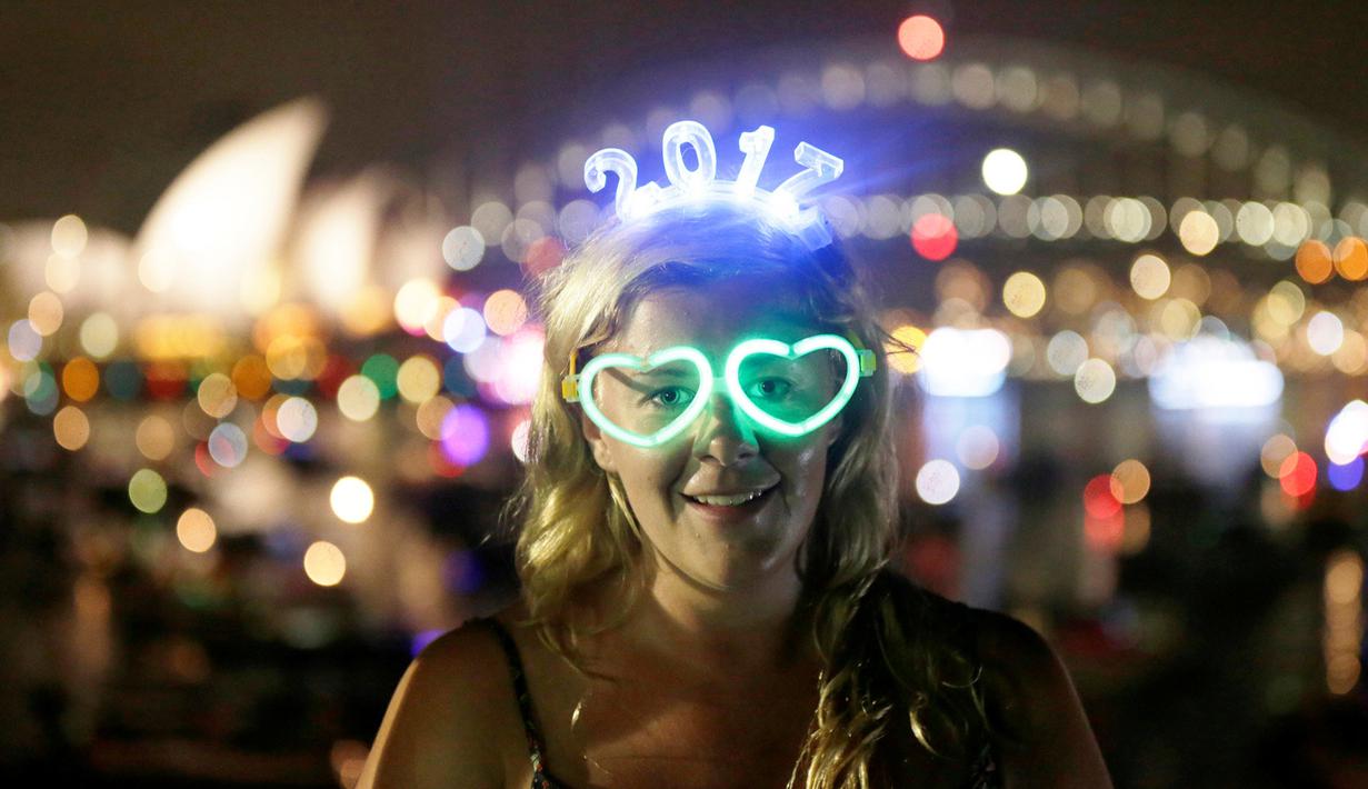 Pengunjung asal Inggris yang bernama Charlotte Kent memakai kacamata bercahaya dan atribut tahun baru saat menyaksikan pesta kembang api di Sydney Opera House dan Harbour Bridge, Sydney, Australia (31/12). (Reuters/Jason Reed)