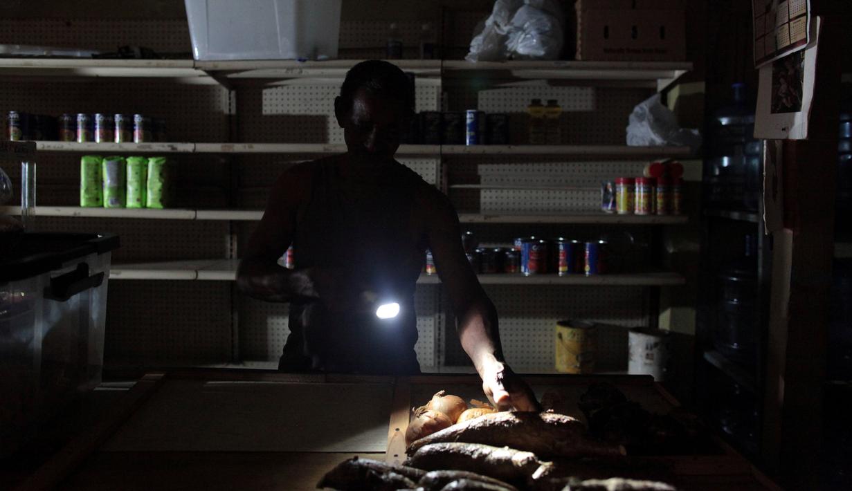 Ramon Ruben menggunakan senter untuk memeriksa tokonya ketika pemadaman listrik di San Juan, Puerto Rico, Rabu (21/9). Kebakaran telah memutus dua jalur transmisi listrik dan mengakibatkan kegagalan penyaluran tenaga ke seluruh pulau. (REUTERS/Alvin Baez)