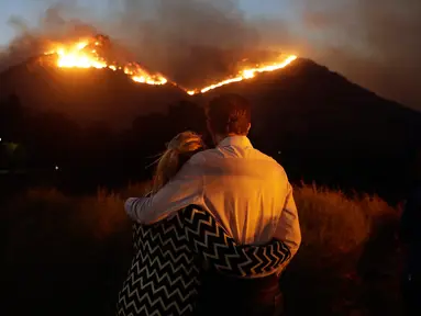 Roger Bloxberg dan istrinya, Anne berpelukan saat menyaksikan kebakaran di puncak bukit dekat rumah mereka di West Hills, California, AS, Jumat (9/11). Api Woolsey melahap ribuan hektare hutan dan menghancurkan banyak rumah. (AP Photo/Marcio Jose Sanchez)