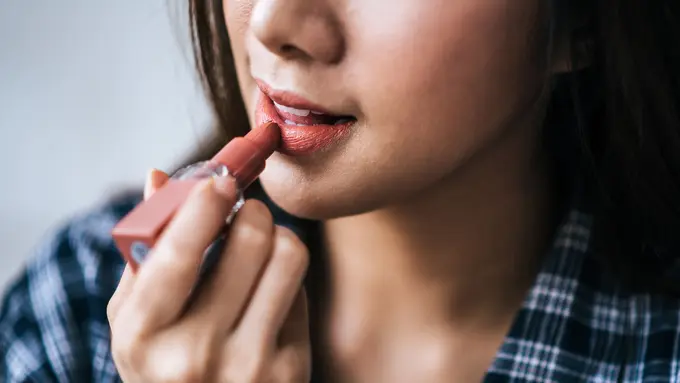 Seorang perempuan sedang mengaplikasikan lipstik di bibirnya (Foto Dok: Freepik/jcomp)