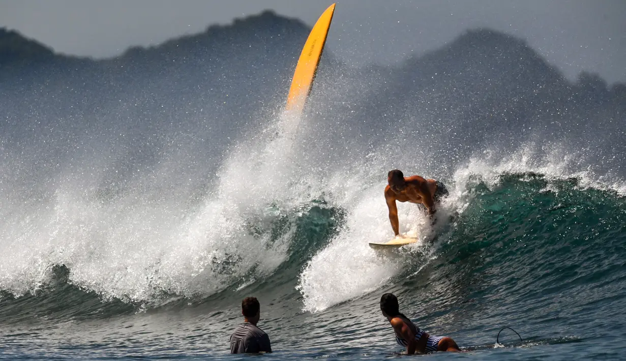 Peselancar menaiki ombak di Pantai Lhoknga, Kabupaten Aceh Besar, Provinsi Aceh, Indonesia, 20 Februari 2023. Karena pesonanya, banyak wisatawan lokal maupun mancanegara selalu ingin berkunjung kembali untuk menikmati segala keindahan pantai ini. (CHAIDEER MAHYUDDIN/AFP)